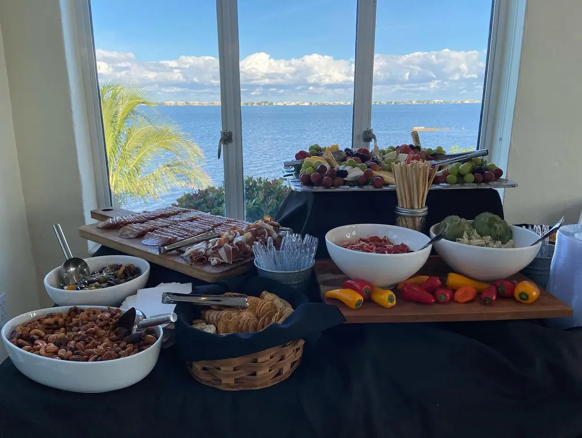 Full buffet line of bowls and trays with a waterfront backdrop